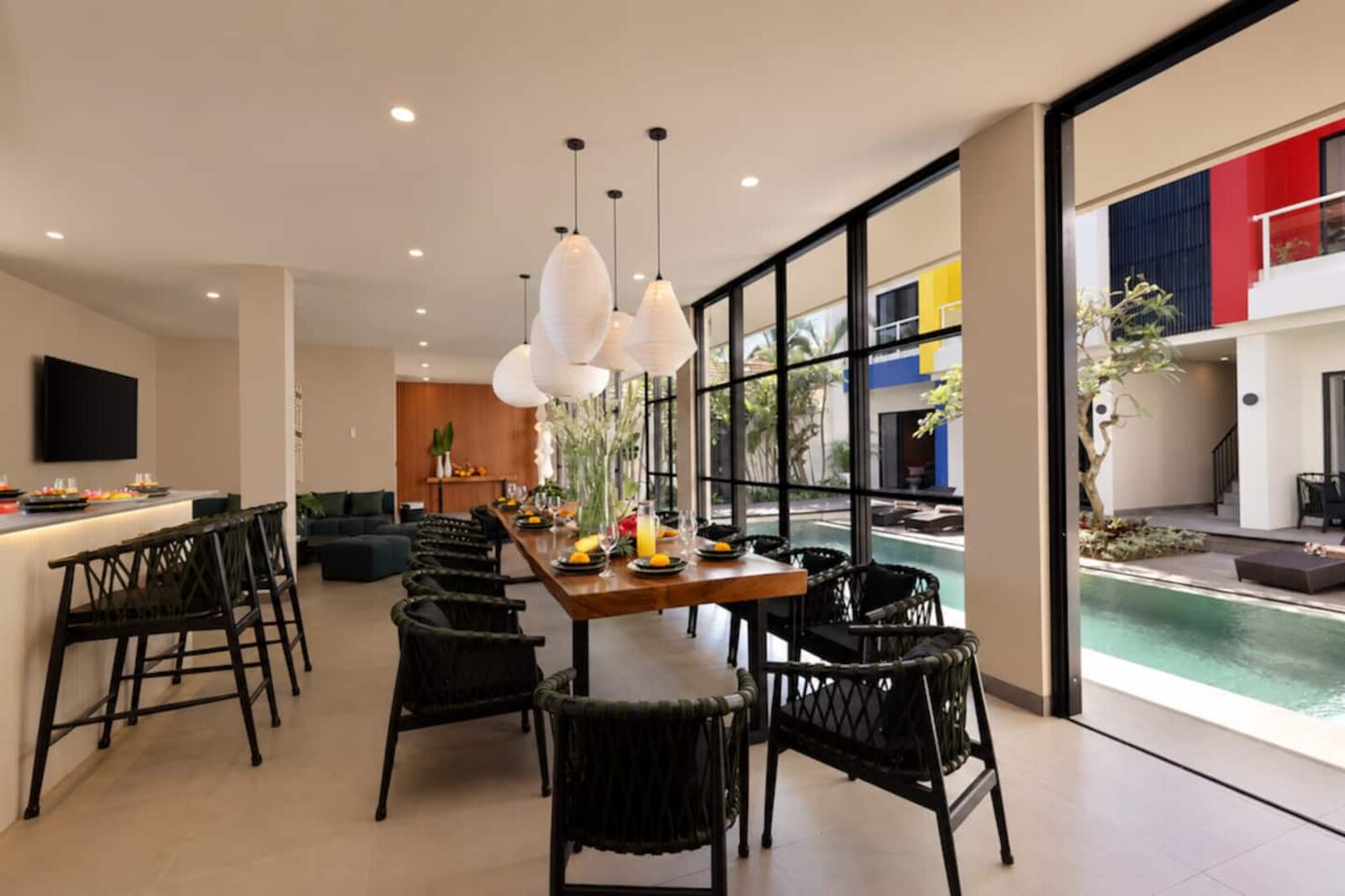 Long dining table beside floor-to-ceiling glass, the pool visible through the opening