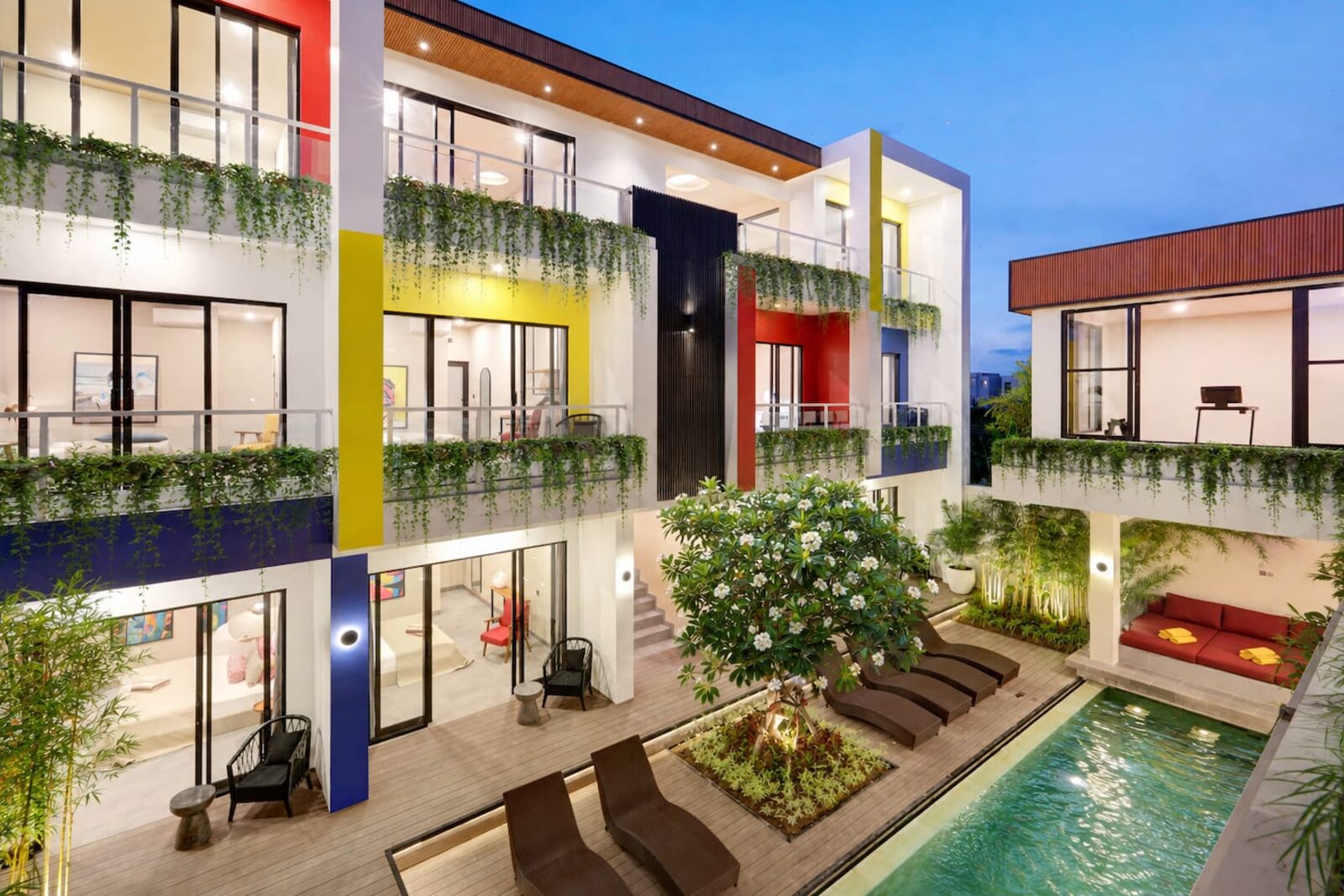 The villa at dusk, three storeys of colour-blocked facade wrapped around a lit courtyard pool
