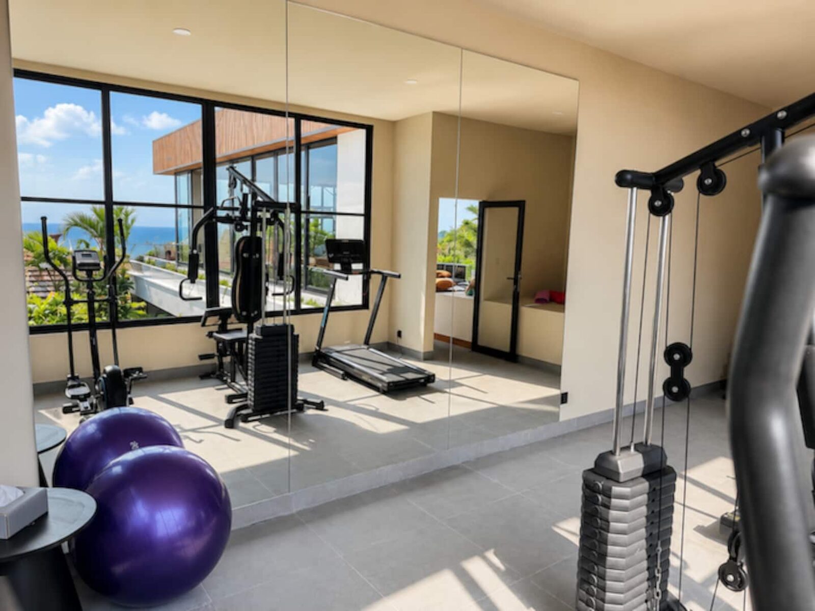 Private gym with cable machine, treadmill and mirrored wall facing the ocean