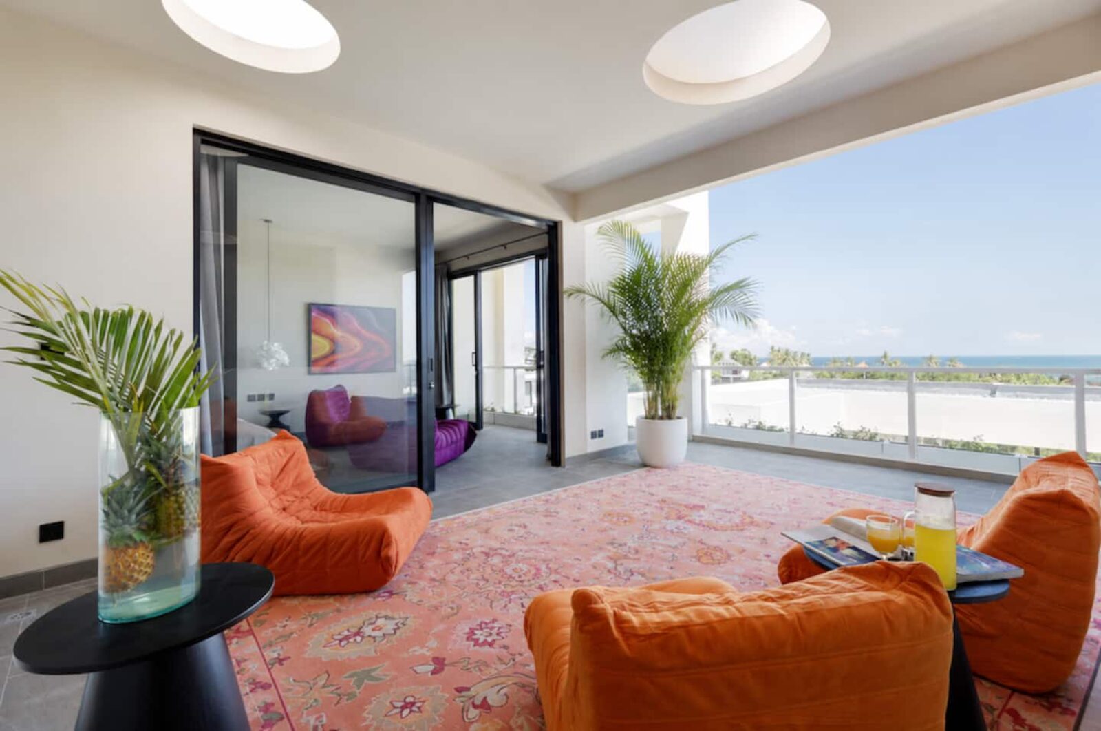 Penthouse living level with low orange lounge chairs on a patterned rug and open terrace doors