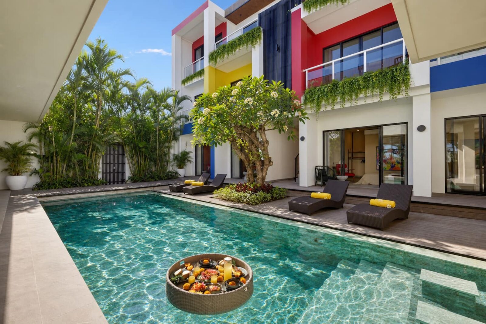 The villa courtyard pool in afternoon light, sun loungers along the deck and palms above the water