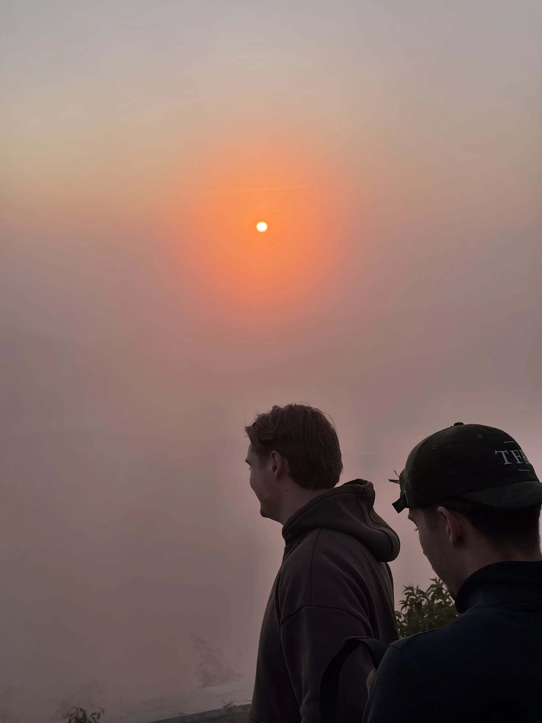 Zwei Teilnehmer blicken im warmen Morgenlicht über Balis Berge, einer trägt eine TFR-Kappe