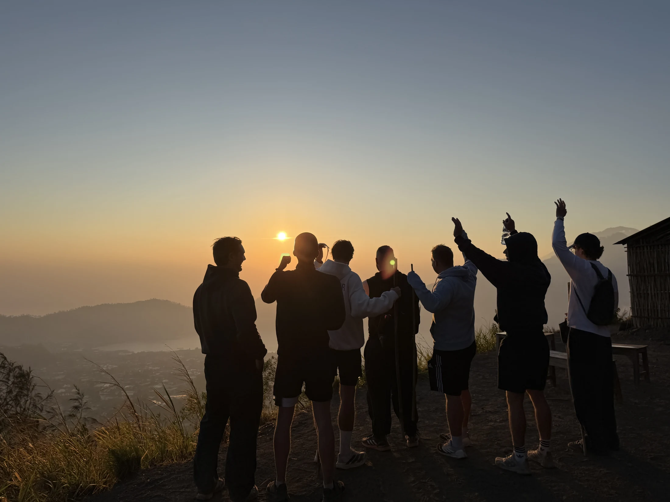 Die Gruppe blickt bei Sonnenaufgang über Balis Berglandschaft und hebt die Arme